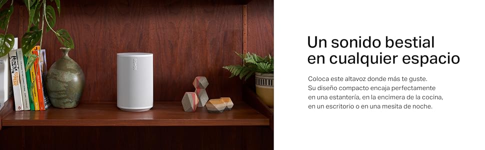 un altavoz inalámbrico blanco en un estante con libros y una planta de fondo.